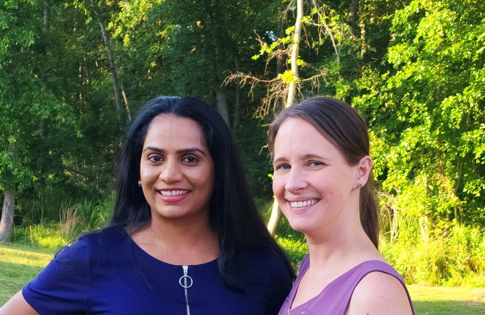 Two smiling women outdoors in a green forest setting